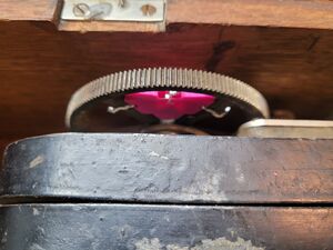 A bright pink 3D printed magnet holder, wired between brass crank spokes.